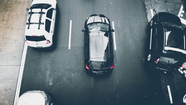 Overhead view of cars on an urban road with wet asphalt, showcasing city transportation.